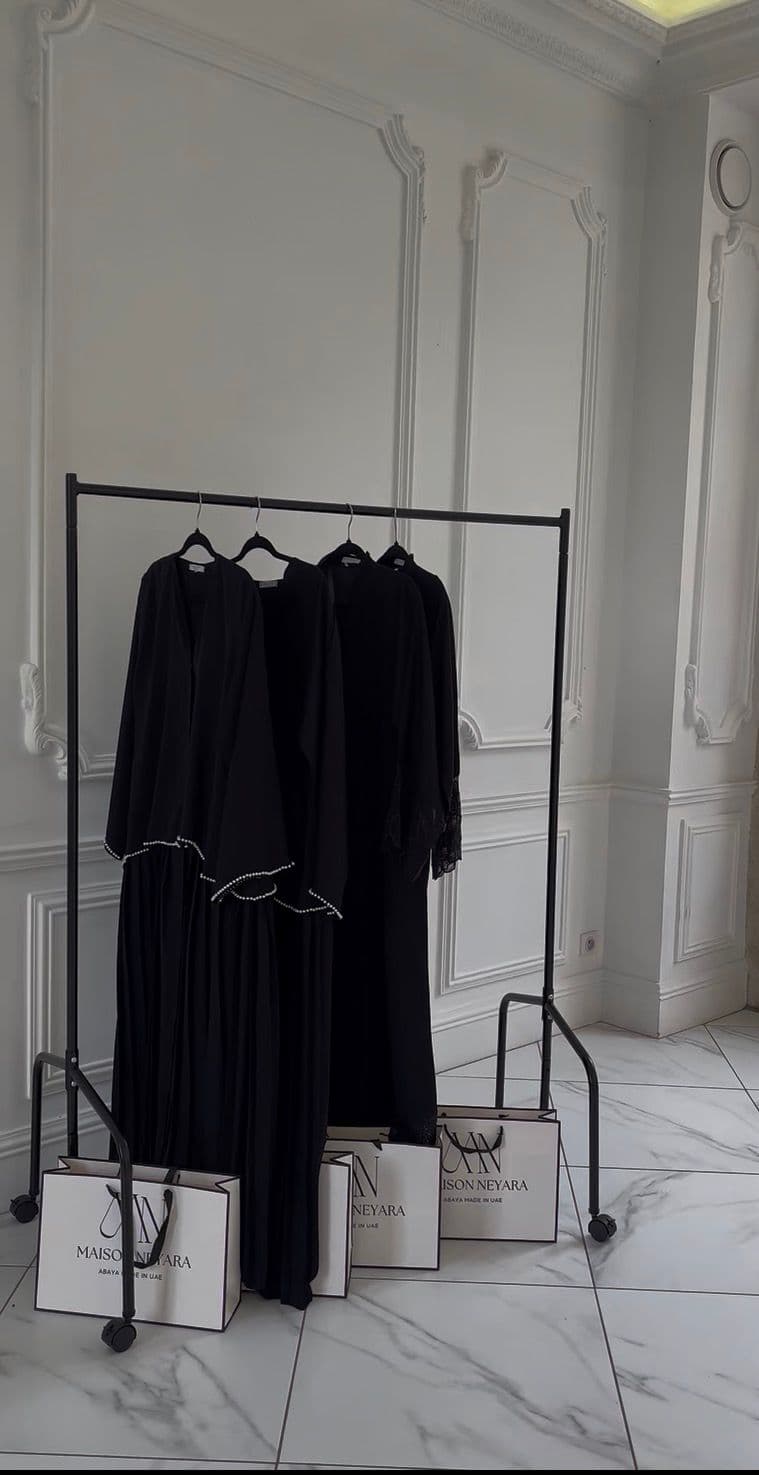 Portant Maison Neyara avec abayas noires et sacs de marque
