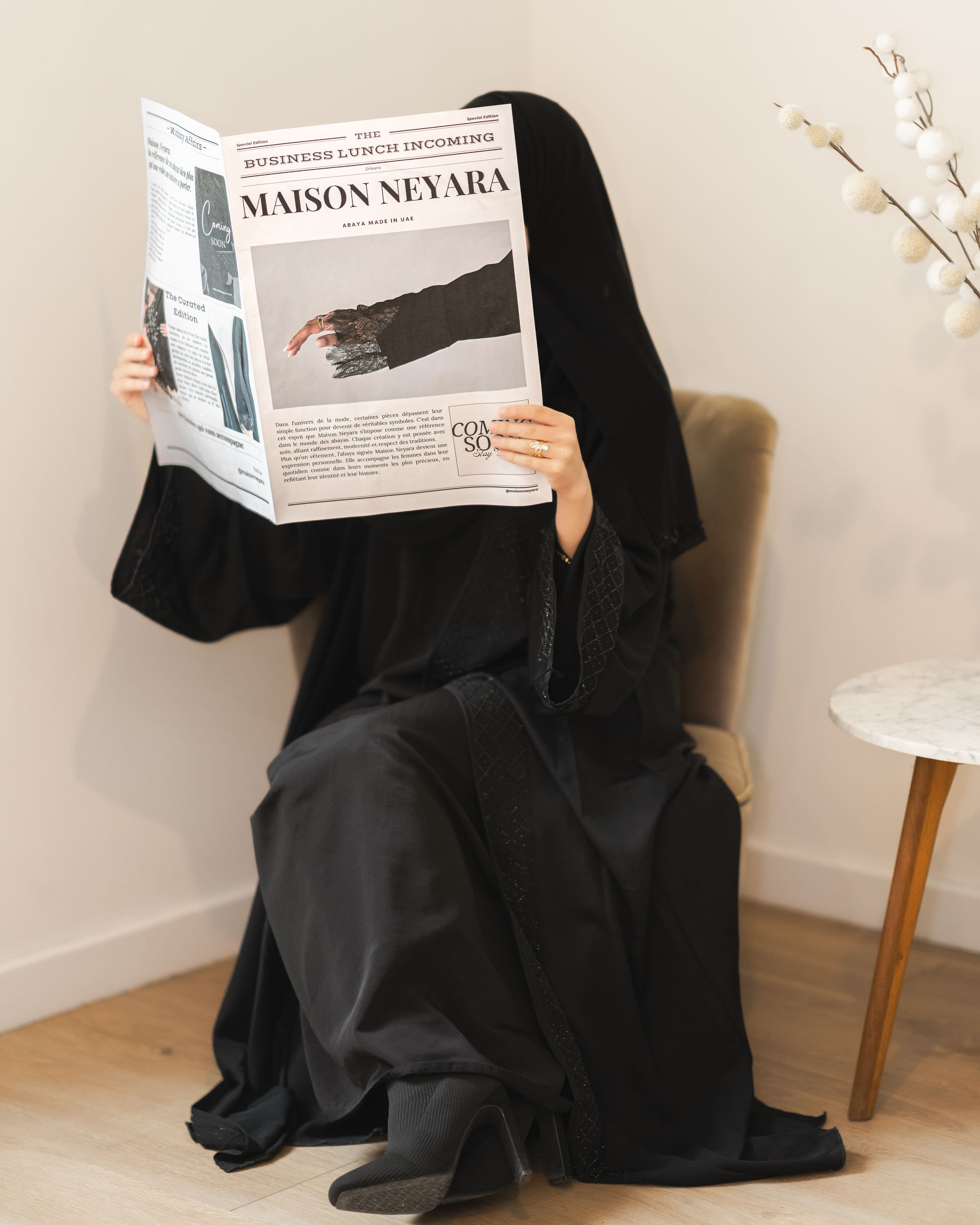 Femme en abaya noire lisant un journal Maison Neyara